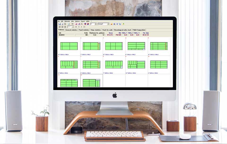 Egy fehér irodai környezetben a fehér irodai asztalon fa kiegészítőkkel egy iMac látható. A monitoron az Ottimo szoftver, azon belül egy táblázatban szabásminták láthatóak.