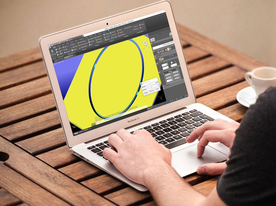Egy fából készült, összecsukható design asztalon egy laptopon dolgozik valaki. A kijelzőn egy sárga háttérben kék 3D-s gyűrű látható.