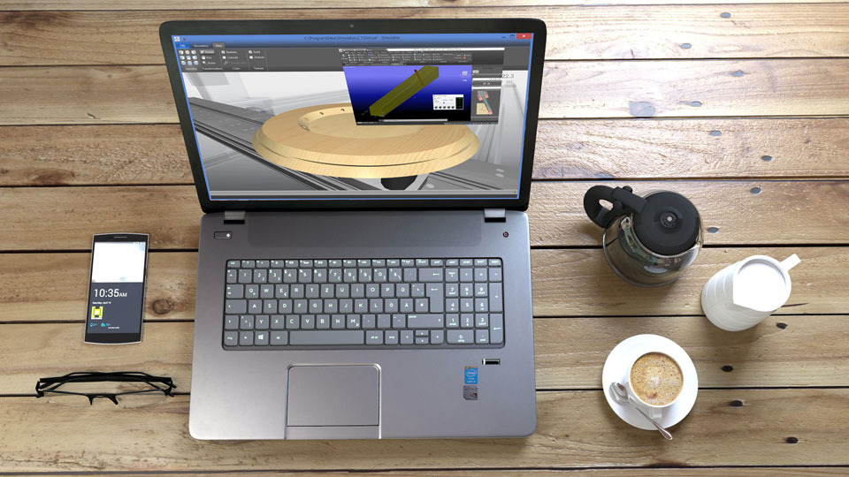 Egy fa asztalon egy laptop jobb oldalán egy kisebb kancsó kévé és tej, valamint egy csésze kapucsínó, a laptoptól balra pedig egy mobiltelefon és egy szemüveg található. A kijelzőn egy kör alakú munkadarab 3D-s képe látható gyártási környezetben.