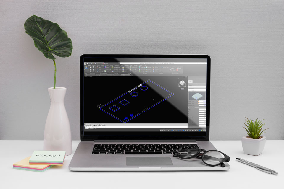 Egy fehér fal előtt, egy fehér íróasztalon egy laptop látható. Rajta hever egy szemüveg, mellette egy toll. A képernyőn a Genio szoftver egy 3D-s CAD ábrája.